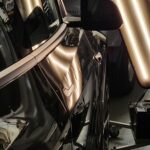 Small dimples from hail damage on the side of a black vehicle shown by a precision hail light.