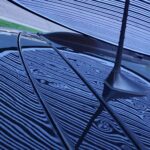 Hail dents showing with a line board during a remote inspection on a black car in someone's front yard.